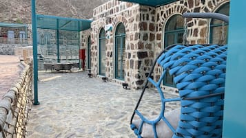 Un edificio de piedra con un área de estar al aire libre techada, una silla colgante y un suelo de piedra.