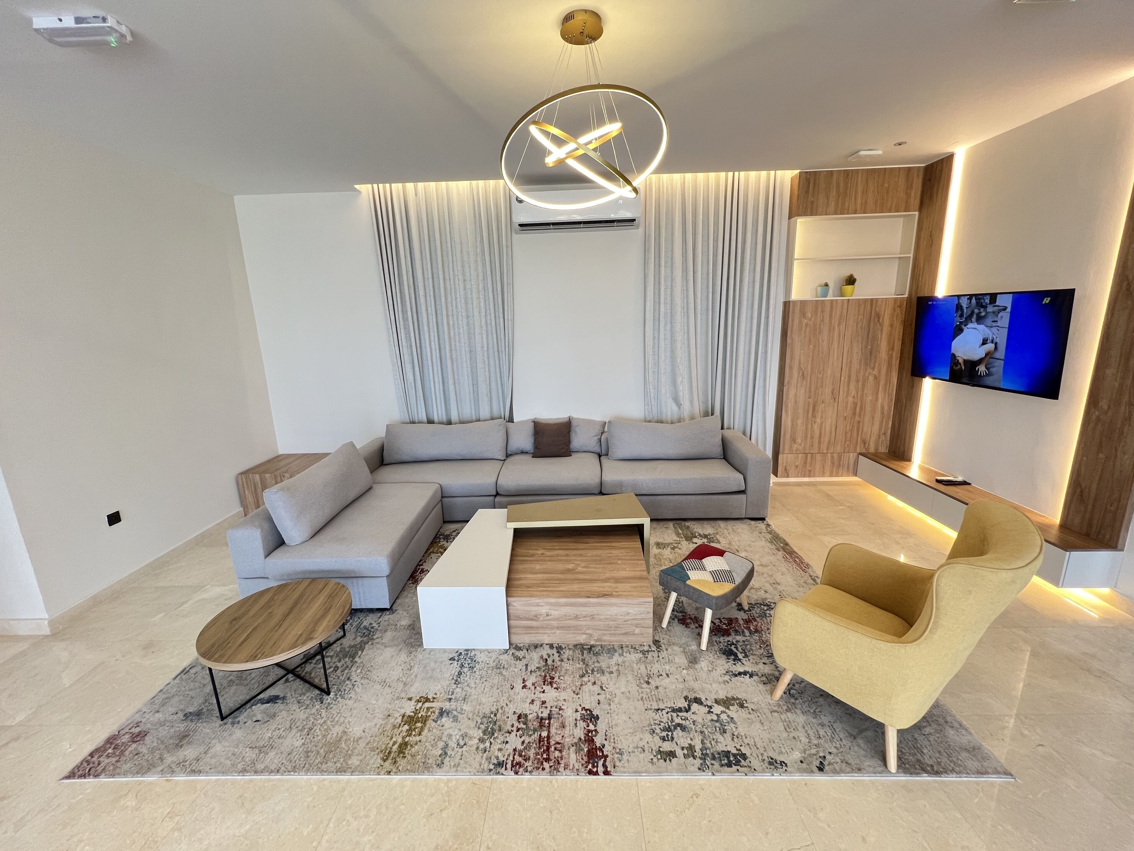 A modern living room with a sectional sofa, a coffee table, a TV, and a unique ceiling light fixture.