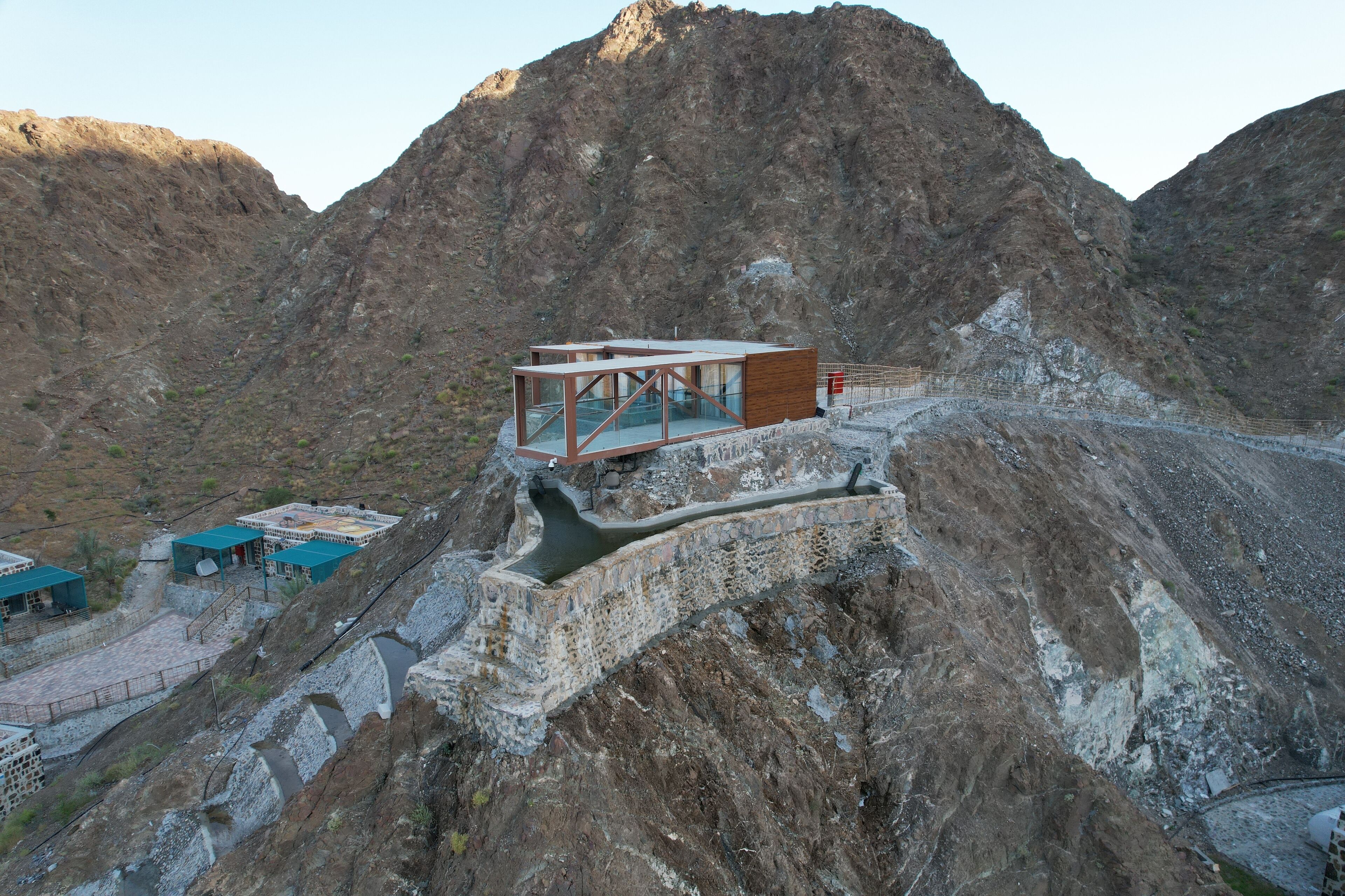A modern building with a glass facade, situated on a rocky hillside with a mountainous backdrop.