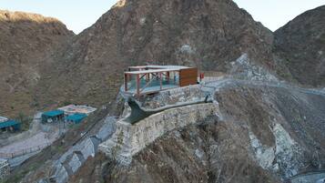 A modern building with a glass facade, situated on a rocky hillside with a mountainous backdrop.