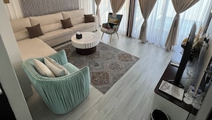 A modern living room with a sofa, armchair, and coffee table. There is a television and a small table with a vase and books.