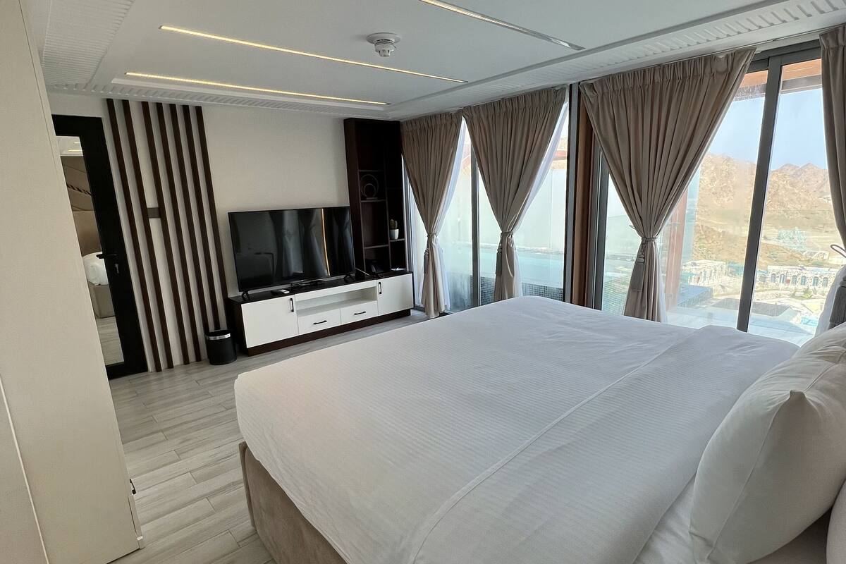 A modern hotel room with a large bed, a TV, and a view of a mountainous landscape.