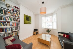 Relax in this spacious living room with a comfortable seating area, bookshelf, and large window offering a view of the outside.