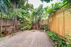 Relax in a serene backyard oasis with a wooden deck, surrounded by lush plants and a majestic palm tree.
