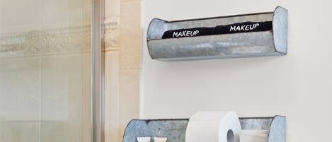 Un baño con puerta de ducha de vidrio, un inodoro con un jarrón blanco de flores secas y dos dispensadores metálicos etiquetados como