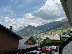 Un borgo montano con case in legno tradizionali, un cielo sereno e vista sulle colline circostanti.