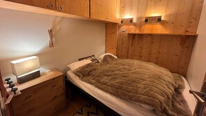 Un dormitorio con paredes de madera, una cama con manta, una mesita de noche con lámpara y una estantería en la pared.