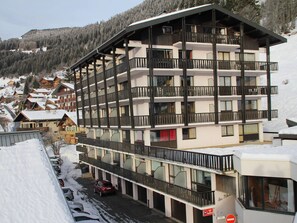 Un hôtel à plusieurs étages doté de balcons, d’un parking et surplombant un paysage montagneux enneigé.