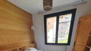 Ett sovrum med en sänggavel i trä, en stor säng med vita sängkläder, ett fönster med utsikt över en byggnad och en garderob i trä.