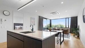 A modern kitchen with a central island, a dining area with a table and chairs, and a large window offering a view of the outdoors.