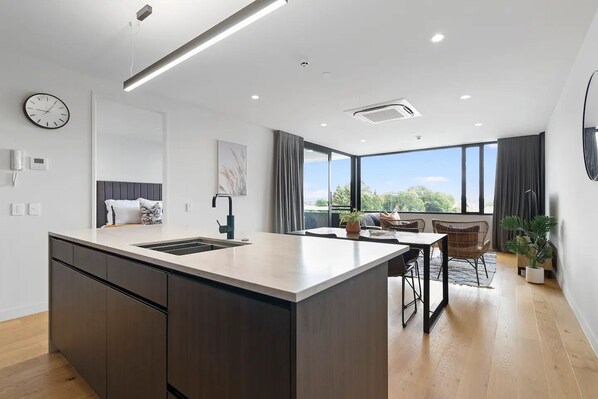 Une cuisine moderne dotée d’un îlot central, d’un coin repas avec une table et des chaises, et d’une grande fenêtre offrant une vue sur l’extérieur.