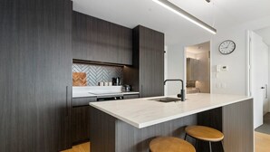 A modern kitchen with dark wood cabinetry, a white countertop, and two wooden stools.