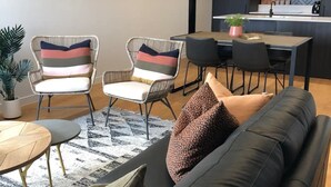 A modern living room with a black leather sofa, two wicker chairs with striped cushions, a small wooden table, and a patterned rug.