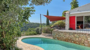 Une piscine bordée de pierres, un mur en pierre et une porte rouge.