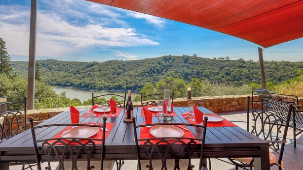 Une table dressée pour quatre personnes, avec une vue pittoresque sur une rivière et des collines en arrière-plan.