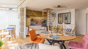 Uma sala de estar moderna com uma mesa de jantar de madeira, cadeiras laranja e rosa, uma escada em espiral e uma janela grande.