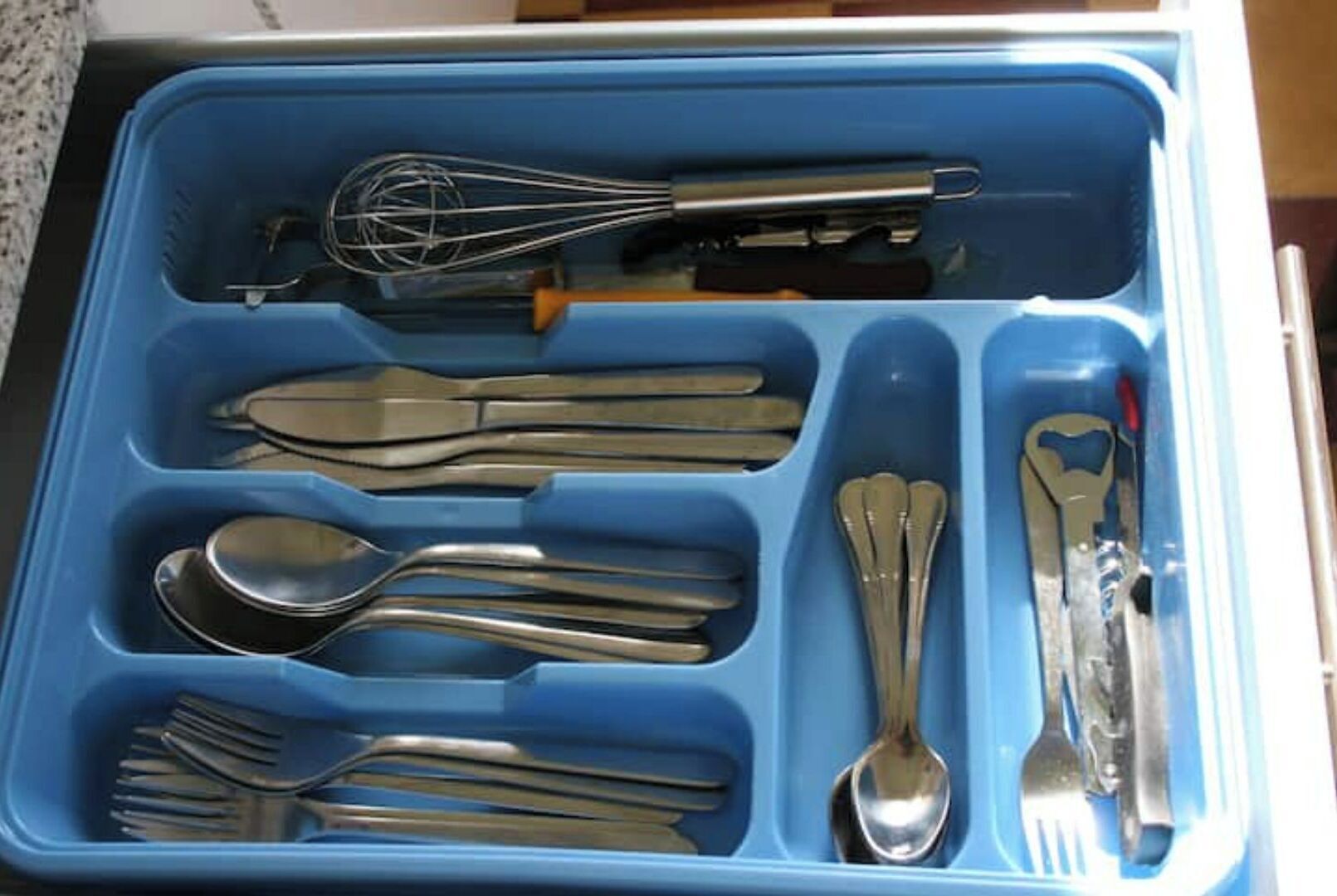 A drawer with compartments containing various utensils including forks, spoons, a whisk, and a pair of tongs.