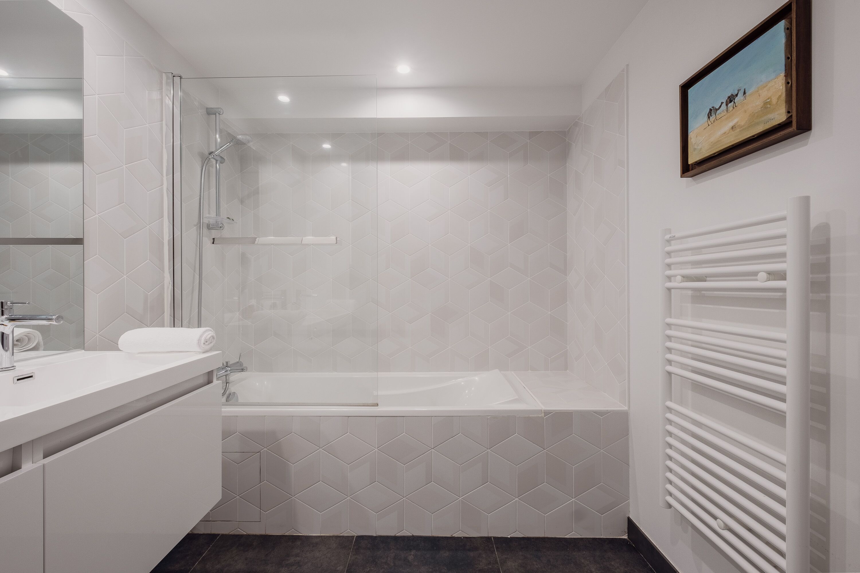 A modern bathroom with a glass-enclosed shower, a white bathtub, and a towel rack.