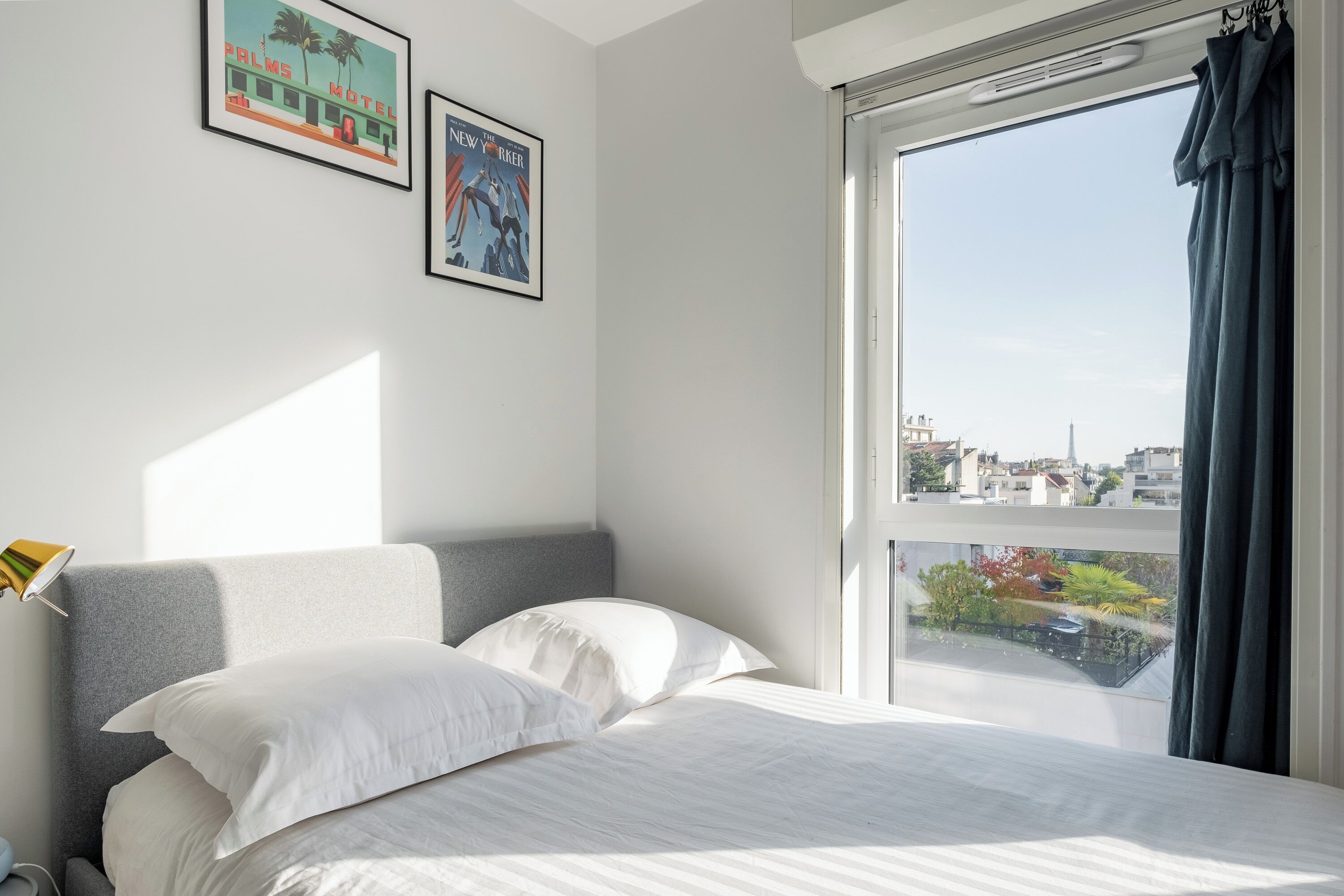 A bedroom with a large window, a bed with white bedding, and two framed pictures on the wall.