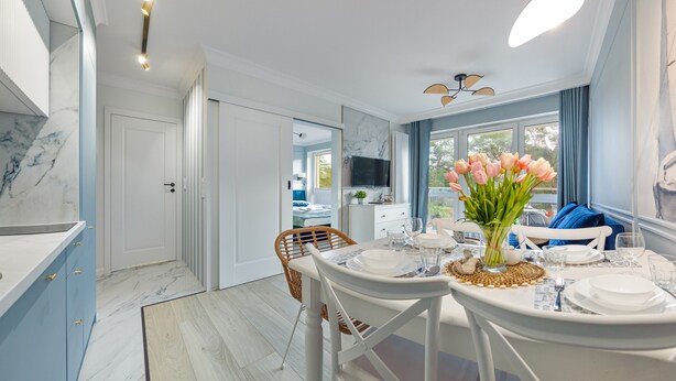 A dining area with a table set for two, a vase of flowers, and a television in the background. - Apartamenty Sun & Snow Wypoczynkowa (Ustka)