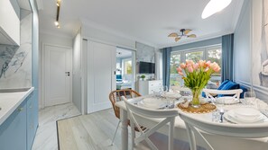 A dining area with a table set for two, a vase of flowers, and a television in the background. - Apartamenty Sun & Snow Wypoczynkowa (Ustka)