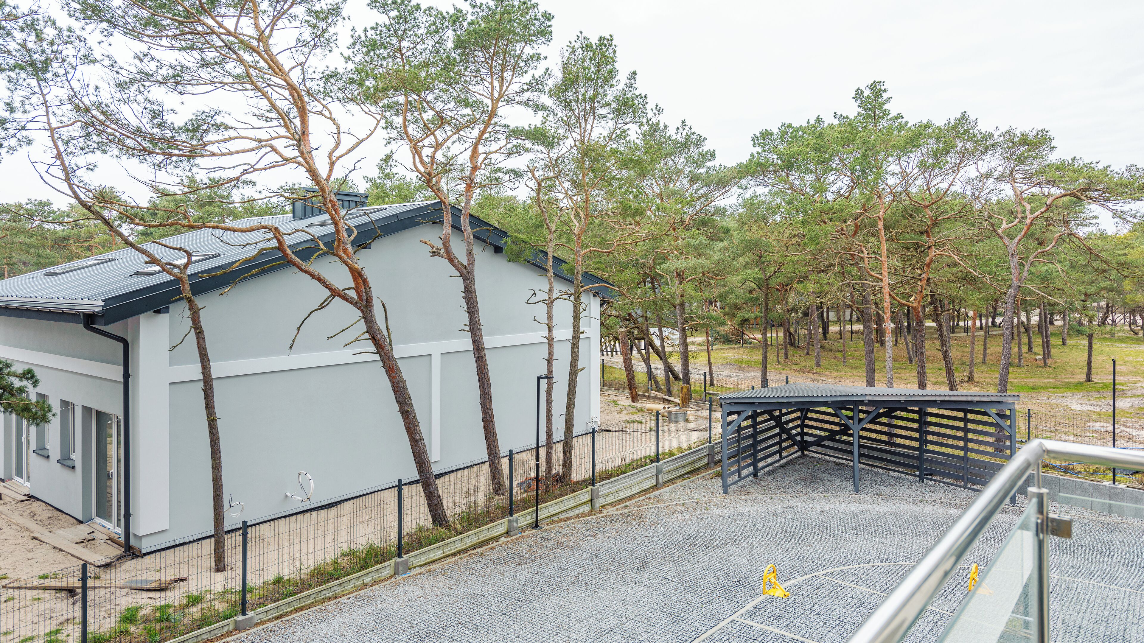 A building with a grey exterior, surrounded by trees and a fenced area.