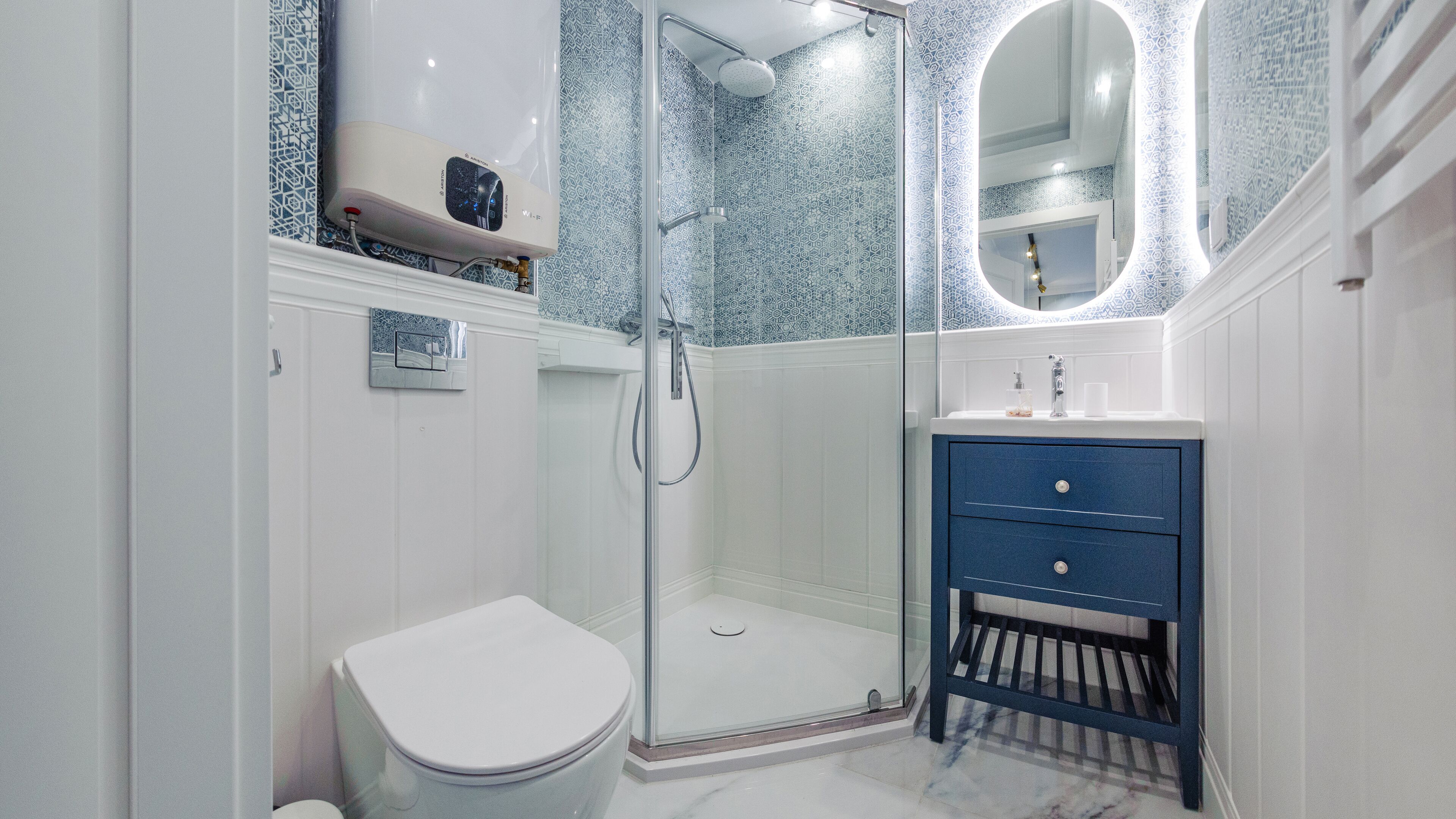 Une salle de bain moderne avec une douche à parois de verre, des toilettes blanches, un meuble-lavabo bleu avec des tiroirs et un grand miroir.