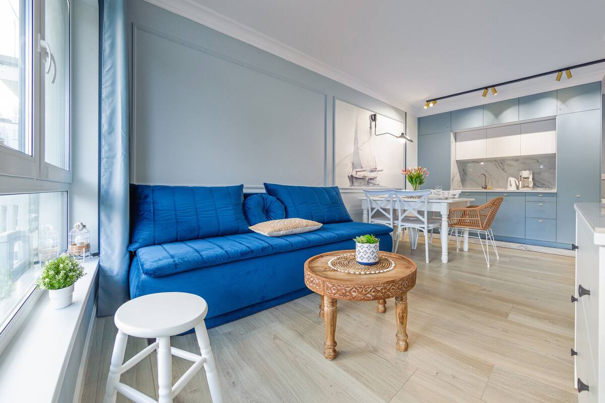 A modern living room with a blue sofa, a wooden coffee table, and a dining area with white chairs.