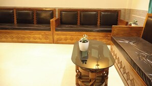 A seating area with a glass-top table, a potted plant, and a cushioned bench. - Hotel Grand Zuri (Agartala)