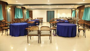 A conference room with round tables and chairs, teal curtains, and a tiled floor. - Hotel Grand Zuri (Agartala)