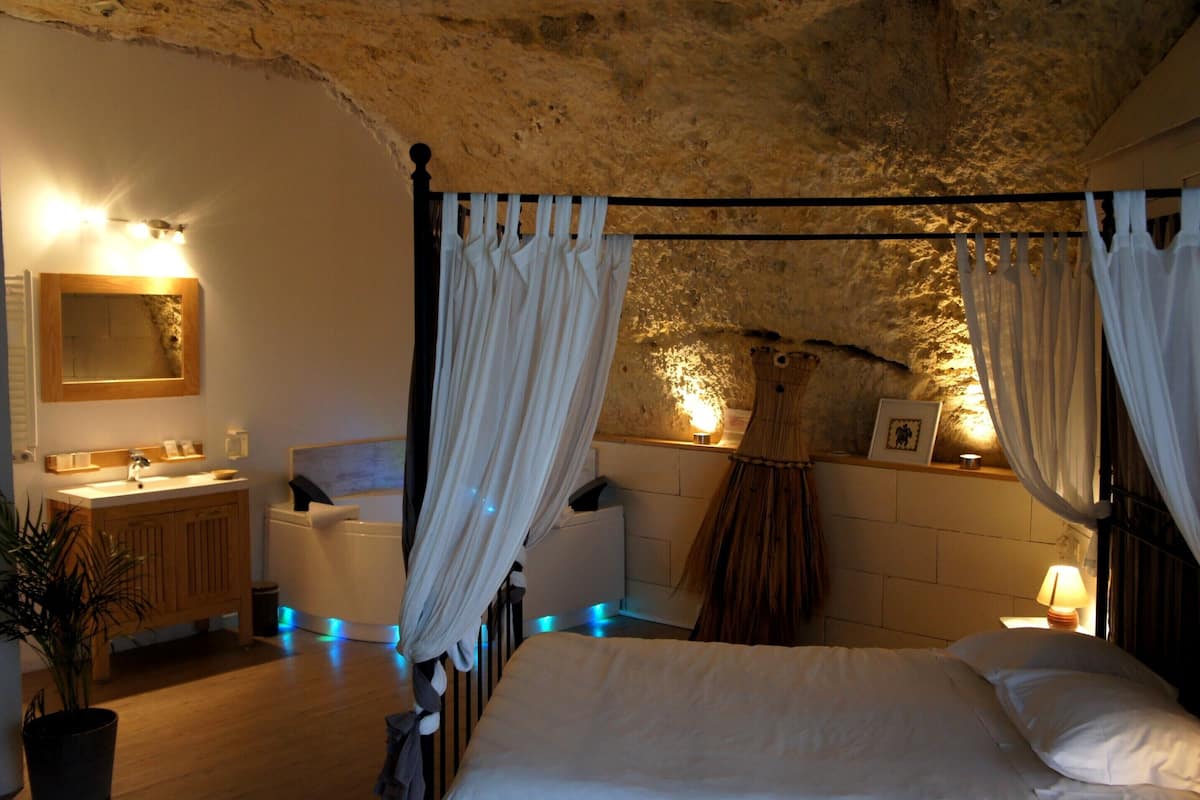 A bedroom with a four-poster bed, a wooden vanity, a mirror, and a bedside table with a lamp.