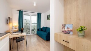 Un apartamento moderno con comedor, sofá, una mesita de noche con lámpara, planta en maceta y un cuadro en la pared.