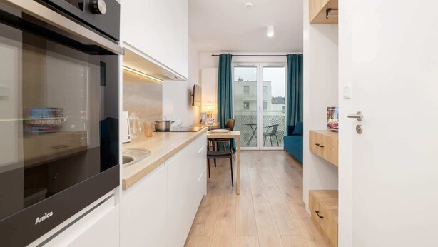Cocina compacta con horno moderno, zona de comedor con mesa y sillas, y vista al exterior a través de un ventanal.