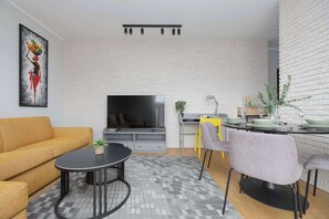 Una sala moderna con un sofá, una mesa redonda de centro, un televisor de pantalla plana y un comedor con sillas y una mesa.
