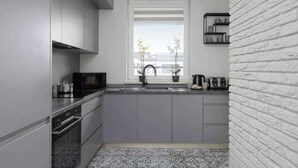 Une cuisine moderne avec des meubles gris, un micro-ondes noir et une fenêtre donnant sur des immeubles.