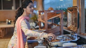 A person serving themselves from a buffet counter with various food items and a bread display. - Brahmi Resort (Doddaballapur)