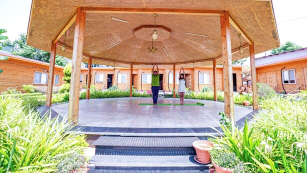 A covered outdoor area with a wooden structure, green mats, and potted plants. - Brahmi Resort (Doddaballapur)