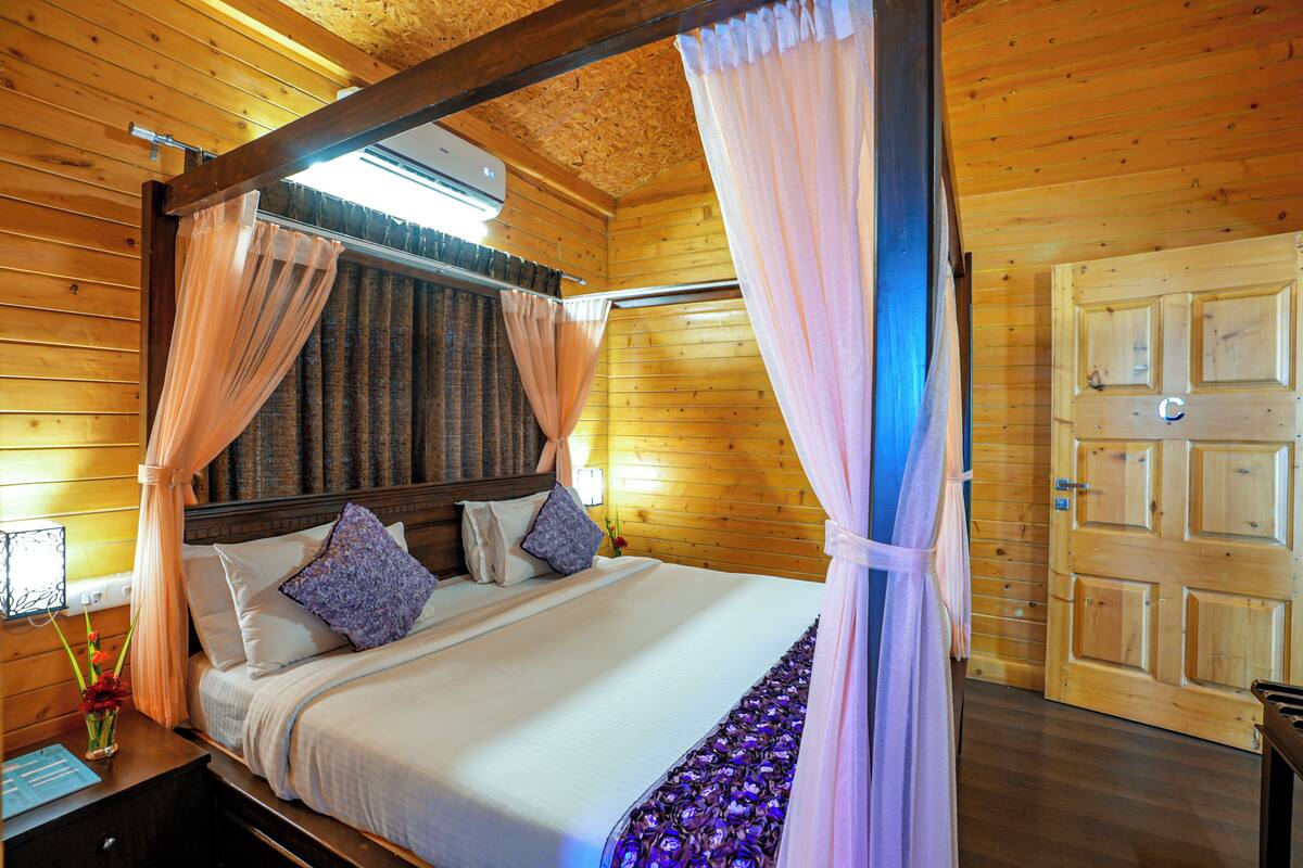 A wooden cabin bedroom with a four-poster bed, a nightstand, and a wooden door.