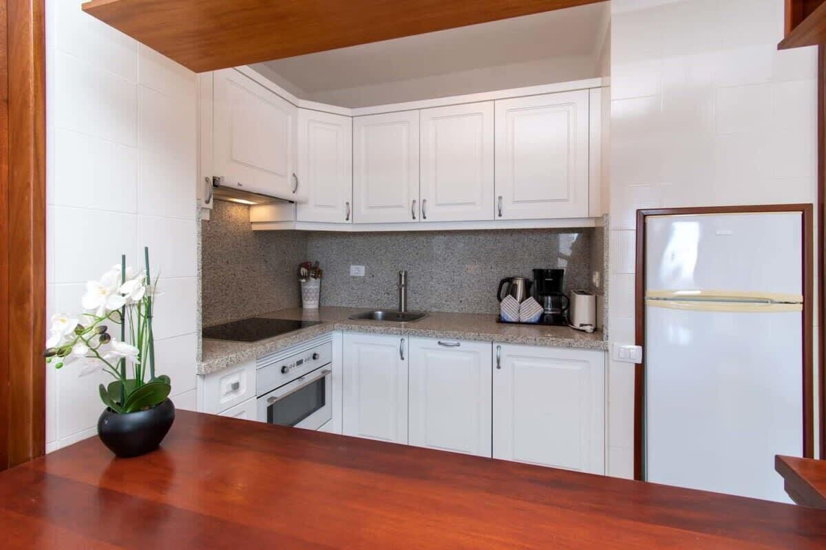 A kitchen with white cabinets, a granite countertop, a stove, and a refrigerator.