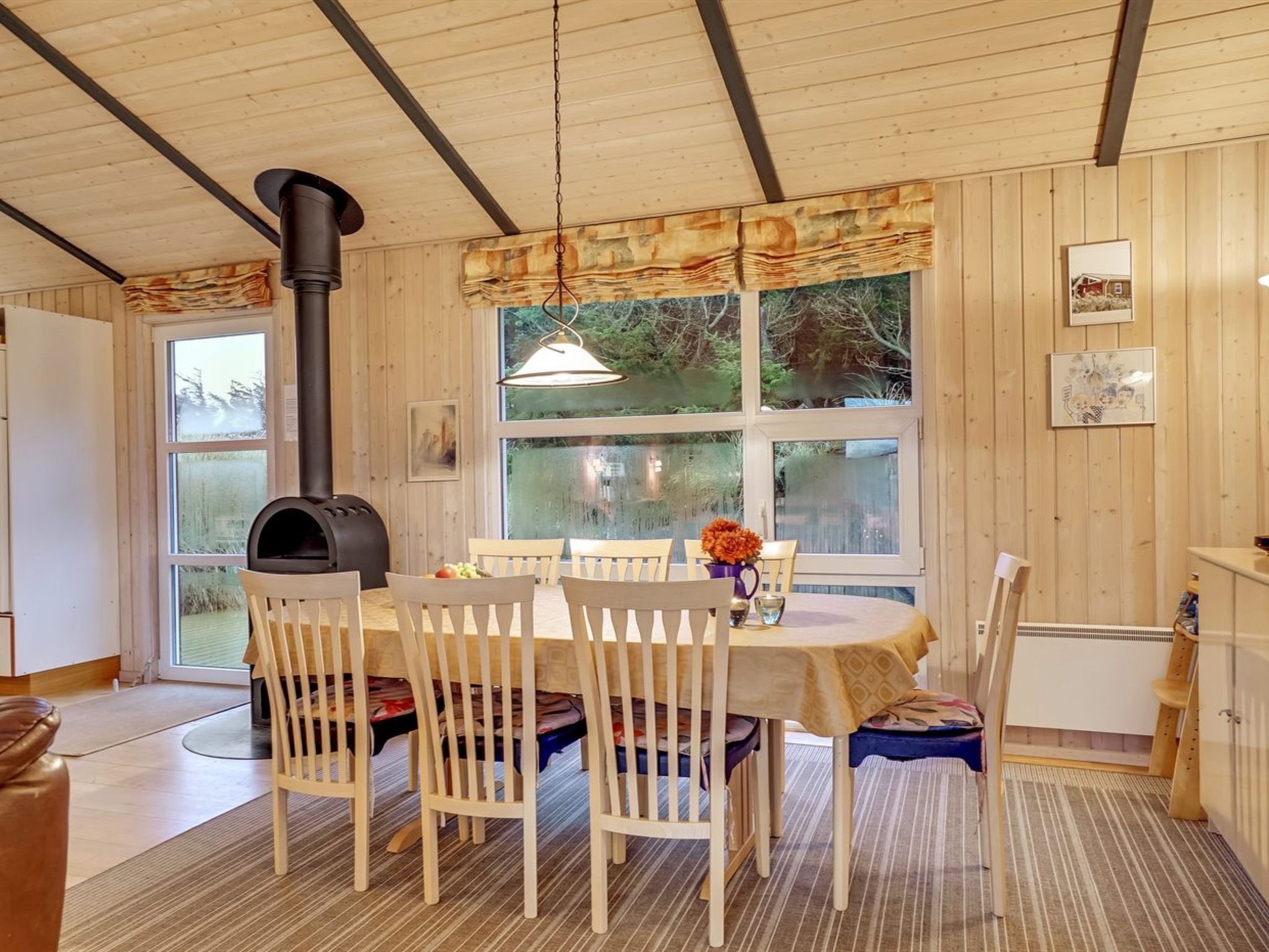 Ein Zimmer mit Holzwandverkleidung, einem runden Tisch, Stühlen, einem Kamin und großen Fenstern.