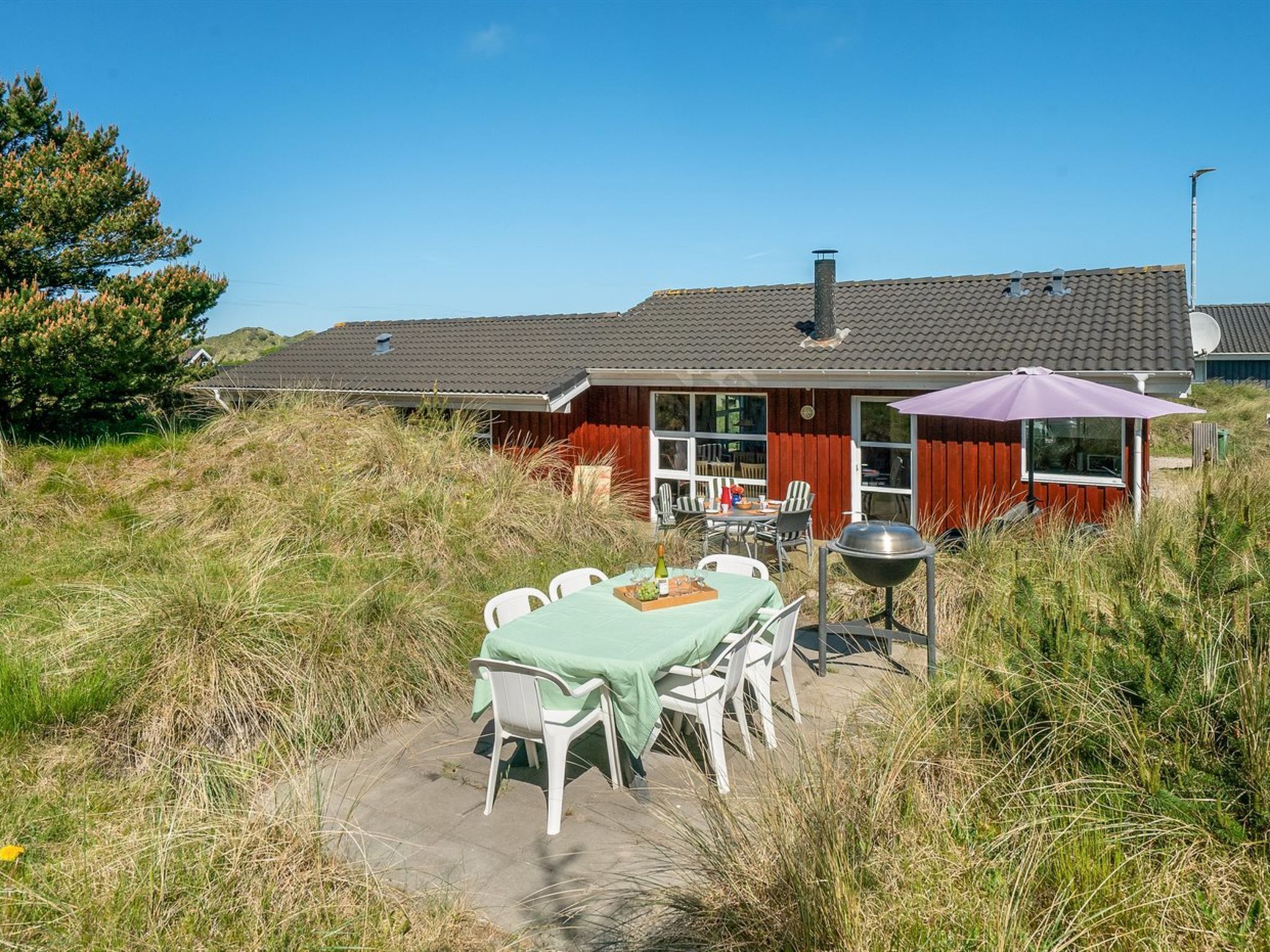 A house with a patio area featuring a table and chairs, a barbecue grill, and a covered seating area with a table and chairs.