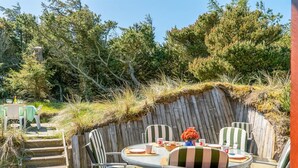 Une terrasse extérieure avec une table ronde et des chaises, entourée d’une plateforme en bois et d’un mur en pierre.