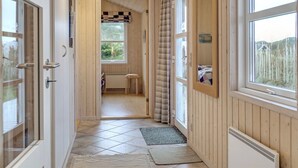 Un couloir aux murs en bois, doté d’un sol carrelé et d’une porte donnant sur une pièce où se trouvent un lit et une fenêtre.