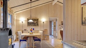 Un intérieur en bois comprenant une table à manger, des chaises, un luminaire suspendu et une cheminée.