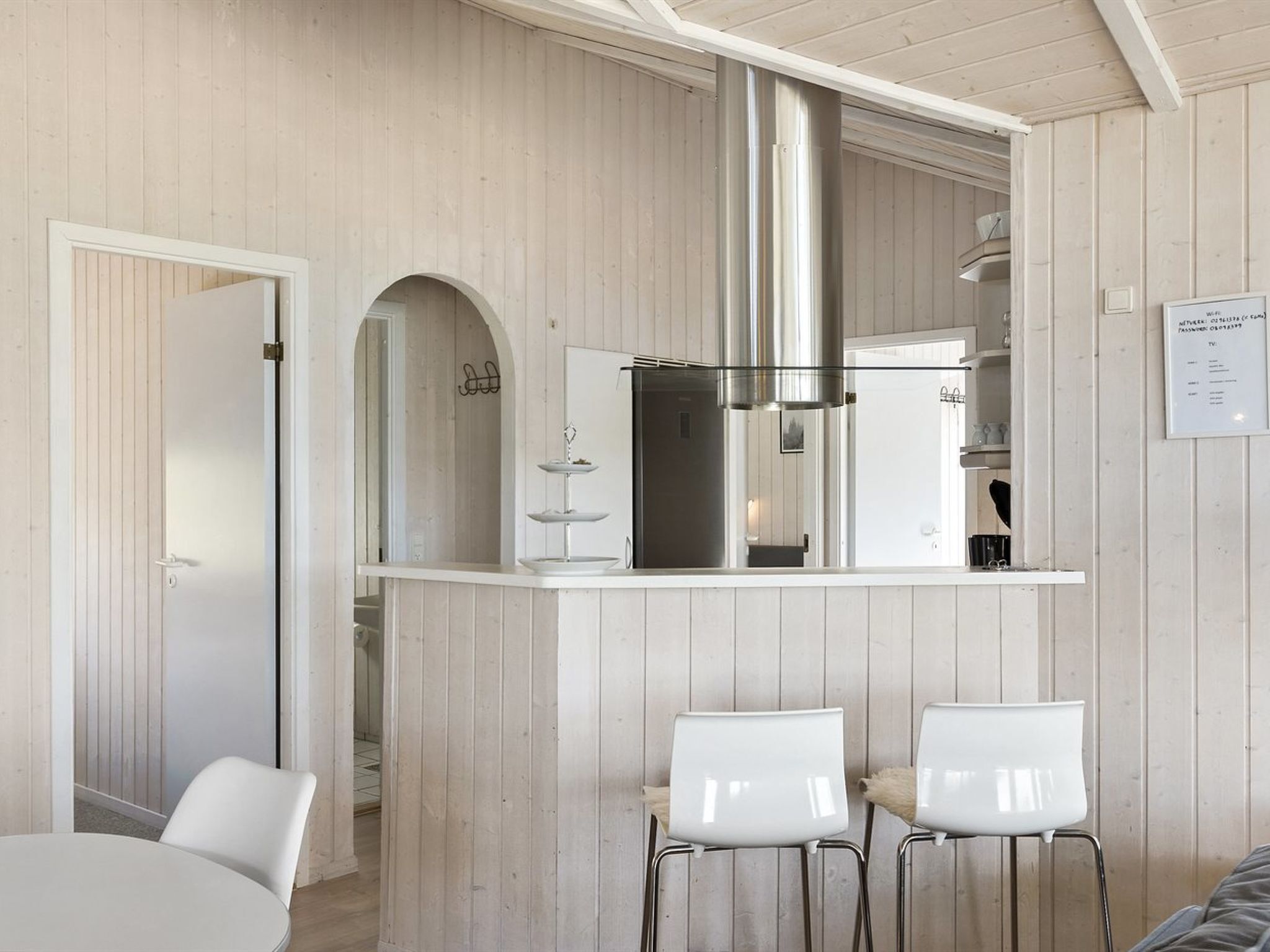 A modern kitchen with a central island, white chairs, and a wooden interior.