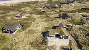 Vista aérea de una zona residencial costera con casas rodeadas de dunas y una playa al fondo.