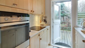 Una cocina moderna con armarios de madera, horno empotrado y ventana con vistas a una terraza.
