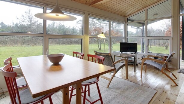 Una habitación amplia con una mesa y sillas de madera, televisión y ventanas grandes que ofrecen vistas al exterior.