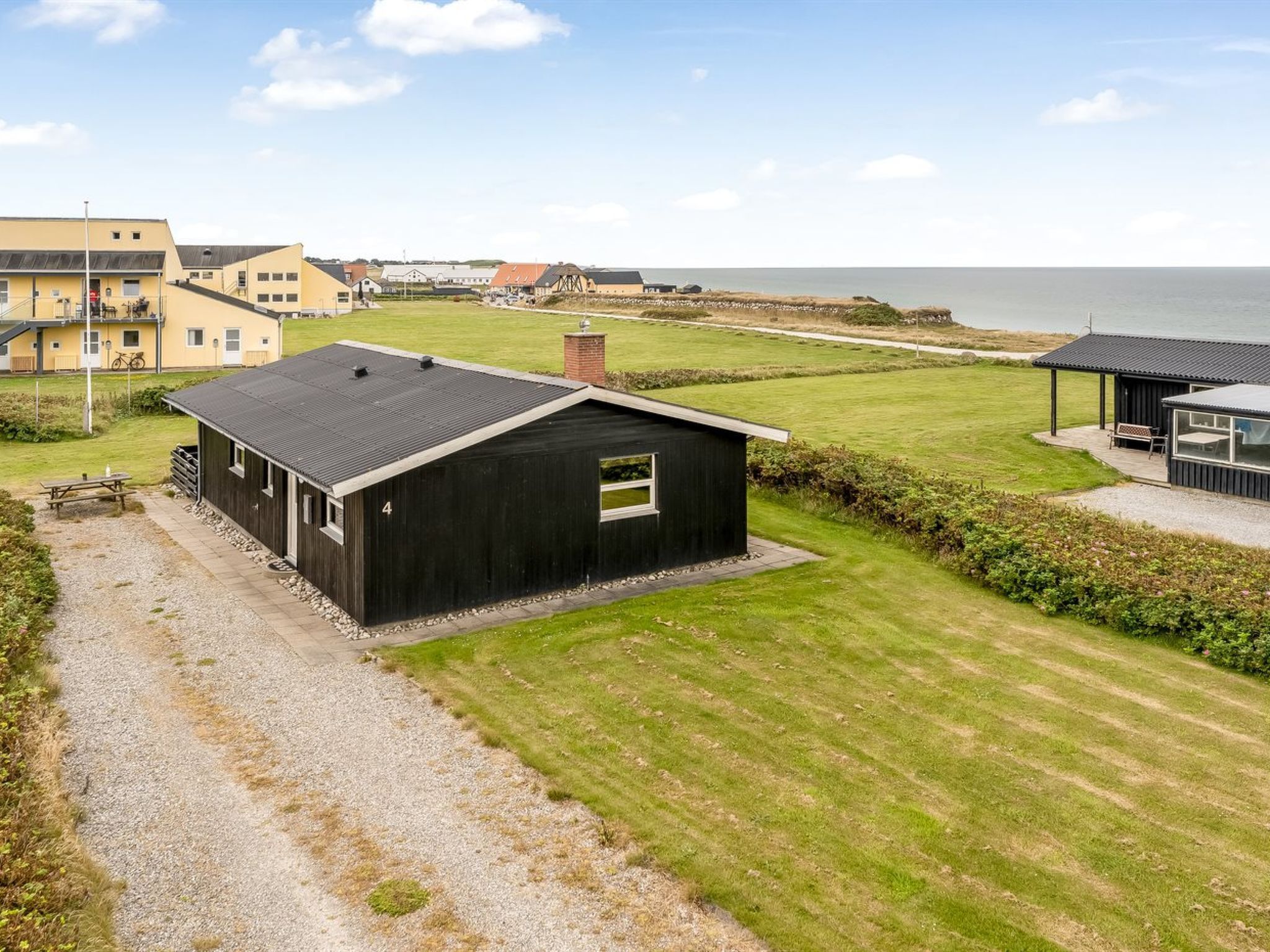 A coastal property with a black building, a gravel driveway, and a grassy lawn.