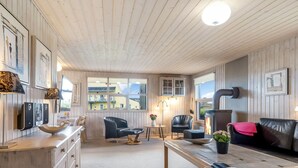 Une pièce chaleureuse avec un plafond en bois, une cheminée, un canapé, une table et une fenêtre donnant sur les bâtiments environnants.